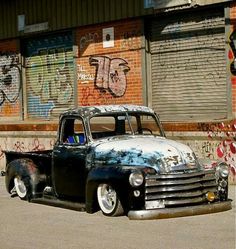 an old black truck parked in front of a building with graffiti on it's walls