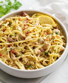 a white bowl filled with pasta and meat on top of a table next to lemon wedges