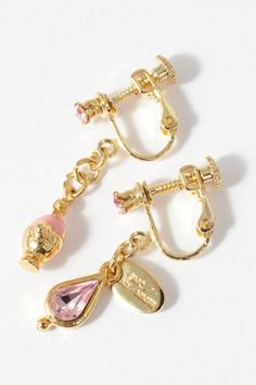 three pairs of gold tone earrings with pink stones and charms on them, one is dangling from the ear