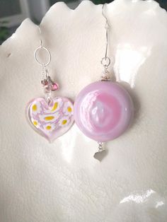 These lovely mismatched earrings are a beautiful shade of opaque pink Venetian Murano glass. The thick blown glass penny bead ( a round bead which has been partially flattened) measures approx 38mm (3.8cm or approx 1.5) and 16mm (1.6cm or 5/8")  It hangs from a Sterling silver oval hoop which in turns hangs from a Sterling silver fish hook earwire and below dangles a small Sterling silver heart. The millefiori glass heart bead measures 34mm (3.4cm or not far off 1.5") It features millefiori to t Heart-shaped Pink Glass Jewelry, Pink Heart-shaped Glass Jewelry, Handmade Pink Glass Jewelry, Pink Glass Jewelry For Jewelry Making, Pink Glass Round Jewelry, Pink Round Glass Jewelry, Unique Pink Round Bead Earrings, Pink Sterling Silver Round Bead Earrings, Adjustable Pink Earrings With Heart Beads