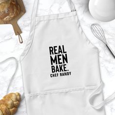 an apron with the words real men bake chef randy on it, next to some croissants