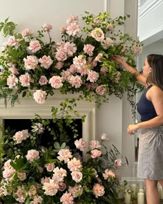 a woman standing next to a fireplace covered in pink flowers