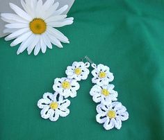 two white crocheted flowers sitting on top of a green cloth next to a flower