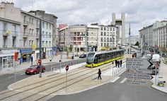 a yellow and black train traveling down tracks next to tall buildings on the side of a road