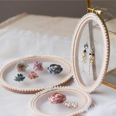 three different types of earrings are in a glass case on a white surface with a gold frame