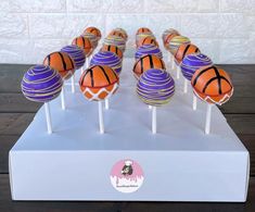 basketball cake pops are lined up on a white display stand with purple and orange frosting