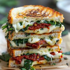 three grilled cheese sandwiches stacked on top of each other with tomatoes and spinach