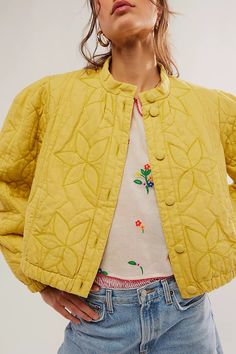 a woman wearing a yellow jacket and jeans with her hands in her pockets, looking off to the side