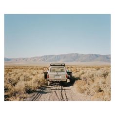 a truck is parked on the side of a dirt road with mountains in the background