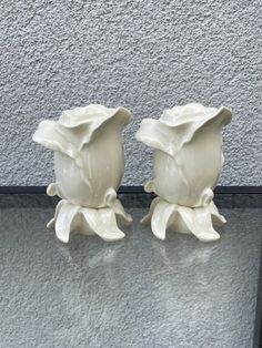 two white vases sitting next to each other on top of a glass table in front of a wall