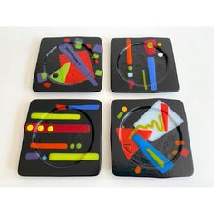 three square coasters with colorful designs on black plastic, one is shaped like a plate and the other has geometric shapes