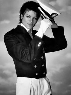 a man in a suit and hat posing for a black and white photo with clouds in the background