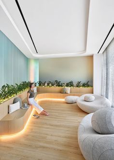 a woman is sitting on a bench in the middle of a room with plants and couches