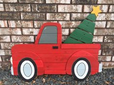 a wooden toy truck with a christmas tree on the back and wheels, sitting in front of a brick wall