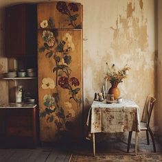 a room with a table, chair and an old refrigerator covered in floral wallpaper