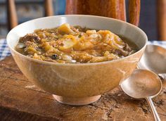 a bowl of soup is sitting on a wooden table with spoons next to it