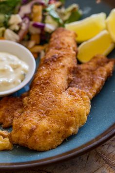 a blue plate topped with fried fish and vegetables next to a bowl of ranch dressing