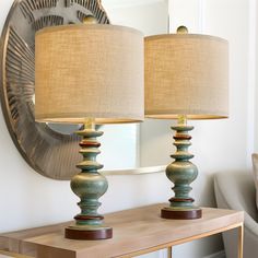 two lamps sitting on top of a wooden table next to a mirror and lamp shade