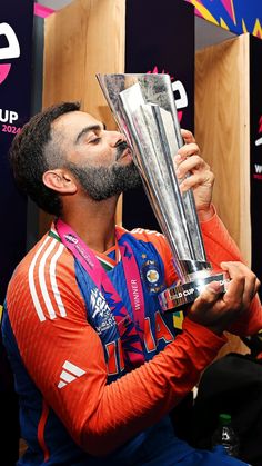 a man holding a trophy in his right hand and looking up at the sky while wearing an orange shirt