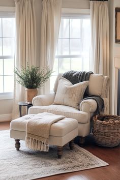 a living room with a chair, ottoman and rug in front of two windows that have white drapes on them