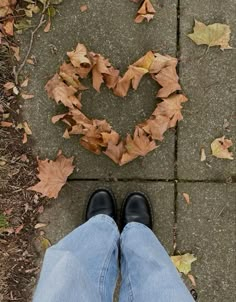 a person standing in front of a heart made out of leaves on the ground with their legs crossed