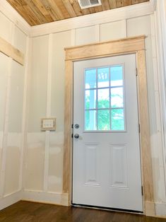 an empty room with a white door and wood paneling on the ceiling, along with a ventilator