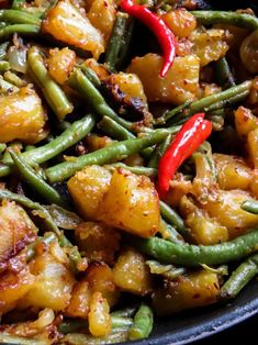 a pan filled with green beans, potatoes and red peppers on top of it's side