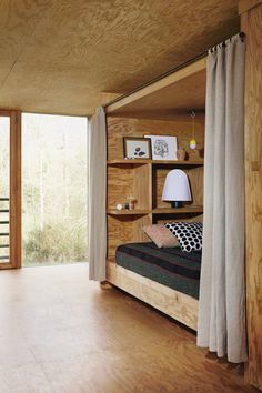 a bedroom with wood paneling and white curtains on the window sill is shown