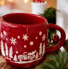 a red mug with white snowflakes and trees on it sitting on a table