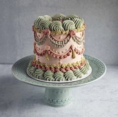 there is a pink and green decorated cake on the plate with silver trimmings