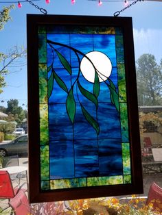 a stained glass window hanging from the side of a building with flowers in front of it