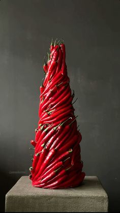 a red christmas tree made out of chili peppers on a block in front of a black wall