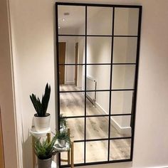 a mirror sitting on top of a wooden floor next to a vase filled with plants