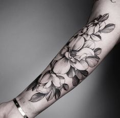 a woman's arm with black and white flowers tattooed on the forearm, in front of a gray background