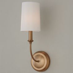 a gold wall light with a white shade on the top and bottom part of it