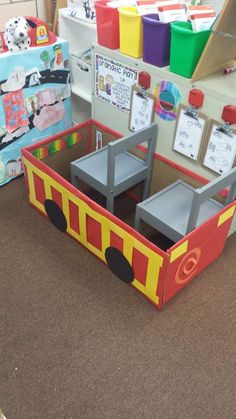 a cardboard firetruck sitting on top of a brown floor next to other toys