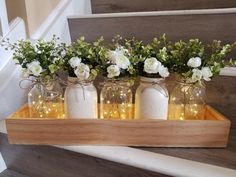 four mason jars with flowers in them are sitting on a wooden tray next to stairs