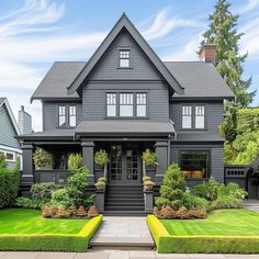 a large gray house with lots of windows and plants on the front lawn in front of it