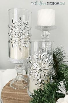 some candles are sitting on a table with pine branches and snowflakes around them