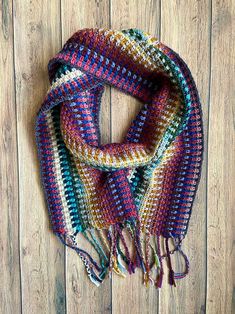 a multicolored crocheted scarf hanging on a wooden wall