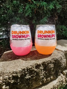 two glasses sitting on top of a rock next to each other in front of trees