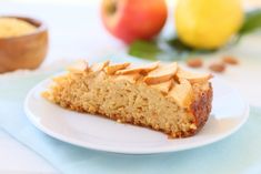 a piece of cake sitting on top of a white plate next to apples and other fruit