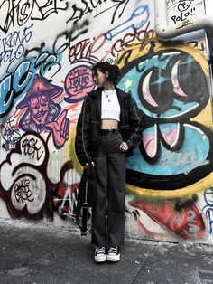 a woman standing in front of a wall covered with graffiti and holding a handbag