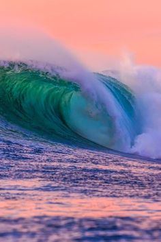 a large wave is breaking in the ocean at sunset or dawn, with pink and blue hues