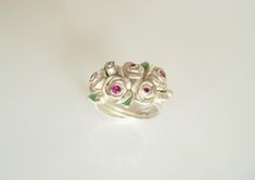 My rose bouquet consists of two larger roses, three medium roses and five buds. Five faceted rubies sparkle in the open flowers. Small transparent green enameled leaves surround the bouquet. The ring band appears to be wrapped from the rose stems. I modeled this unique piece in wax and had it cast in recycled 925 silver (lost shape). The rose bouquet has a ring width of 56 and can be brought to a width of 57. The bouquet of roses, which never withers, is delivered in a nice black jewelry box. Silver Wedding Ring With Roses, Silver Flower Ring With Roses For Wedding, Fine Jewelry Rose Design Ring, Elegant Sterling Silver Rings With Roses, Elegant Silver Rings With Rose Details, Silver Flower Ring With Roses For Gift, Rose Flower Sterling Silver Wedding Ring, Rose Color Sterling Silver Flower Ring For Wedding, Rose Flower Ring In Sterling Silver For Wedding