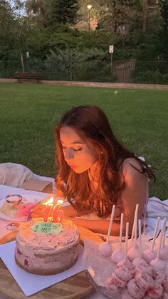 a woman sitting at a table with a cake and candles in front of her on the grass