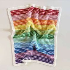 a multicolored crocheted dishcloth is displayed on a white surface