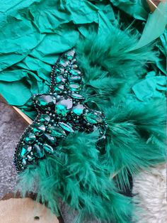 a green feather and beaded brooch laying on top of a piece of wood