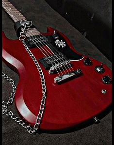 a red electric guitar with a chain attached to it's neck, sitting on the ground