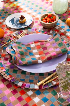 the table is set with plates, silverware and oranges